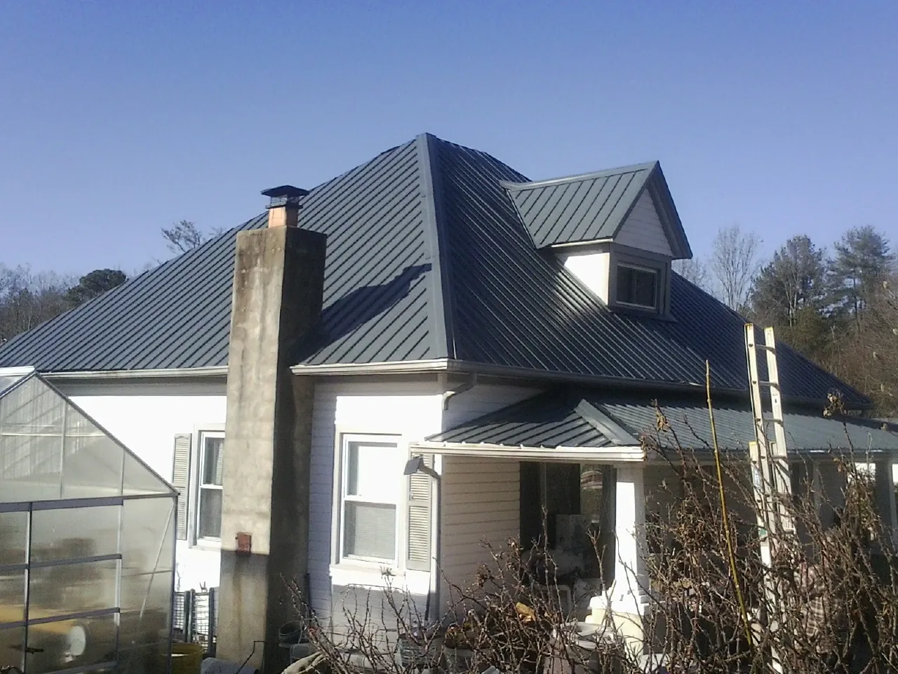 Dark blue standing seam metal roof on a white farmhouse with dormer — Slate & Tile Roof Repair by Roofing Brothers in Brownville