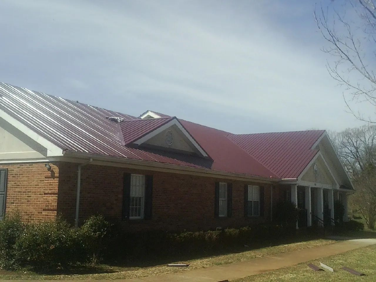 Red metal roof with gabled entries on a long brick building, from a Hail Damage Roof Repair job in Brownville