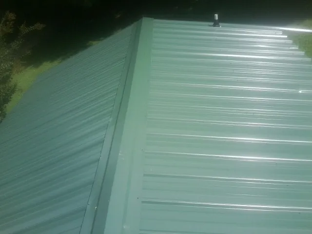 New green metal panels meeting at the ridge of a roof — Flat Roof Repair work by our crew in Brownville