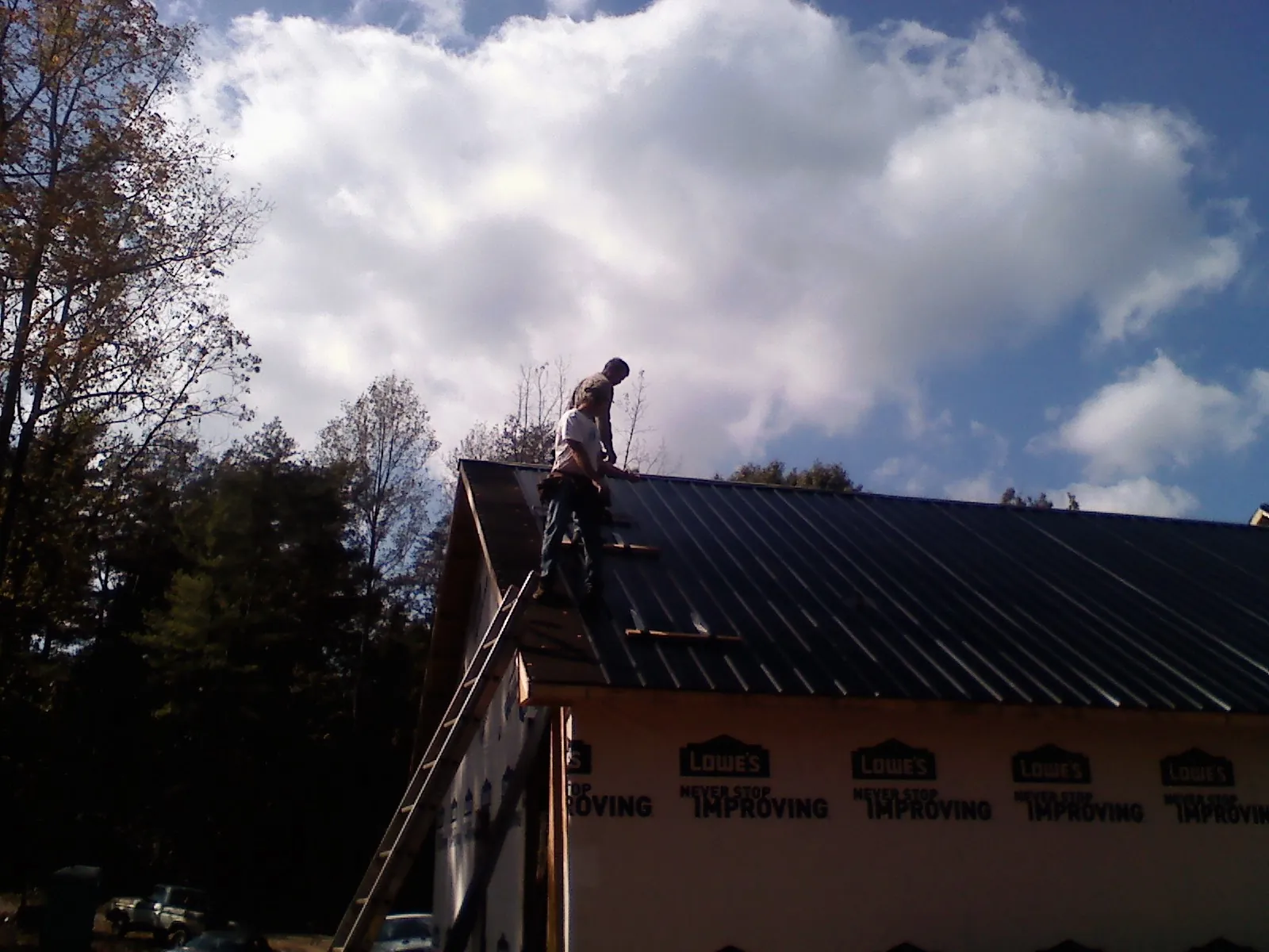 Roofer fastening dark metal panels high against a cloudy sky, from a Roof Inspection job in Brownville