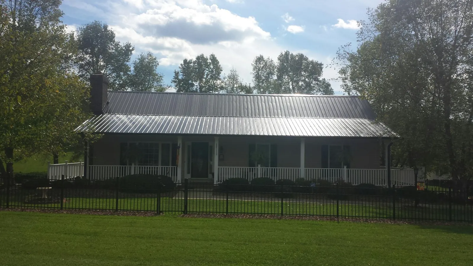 Gray metal roof on a brick ranch with a full width front porch — Gutter Guard Installation work by our crew in Brownville