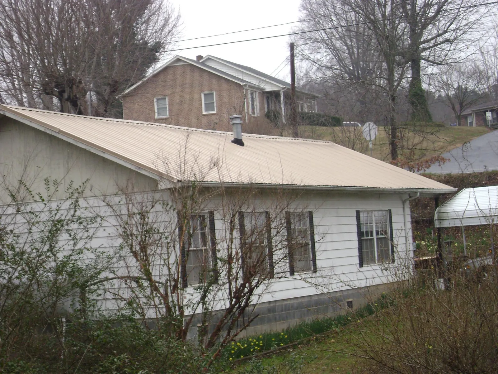 Tan metal roof on a white sided house set into a hillside — Commercial Roofing by Roofing Brothers in Brownville