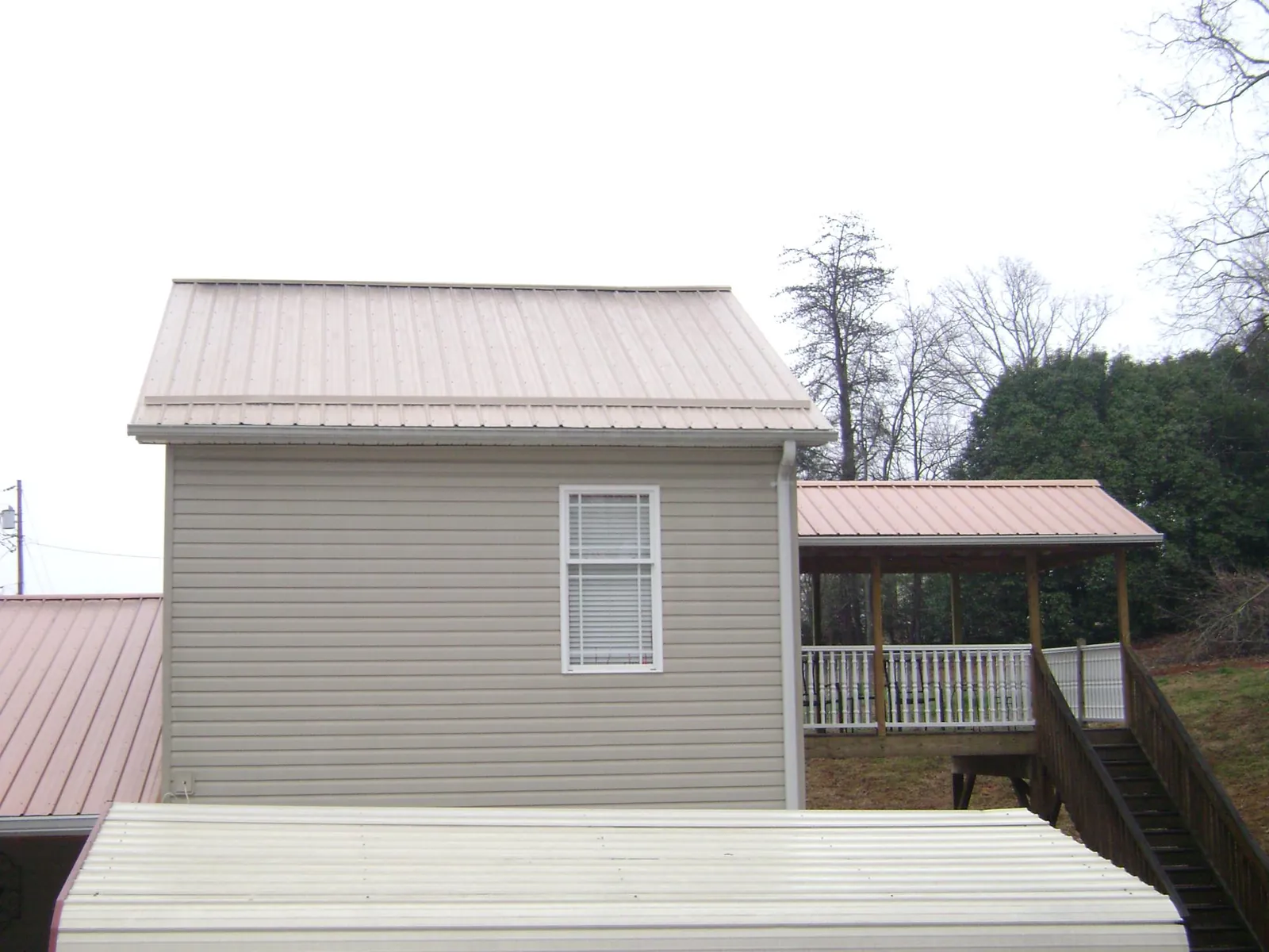 Tan metal roofs on a two story addition and attached porch, from a Roof Replacement job in Brownville